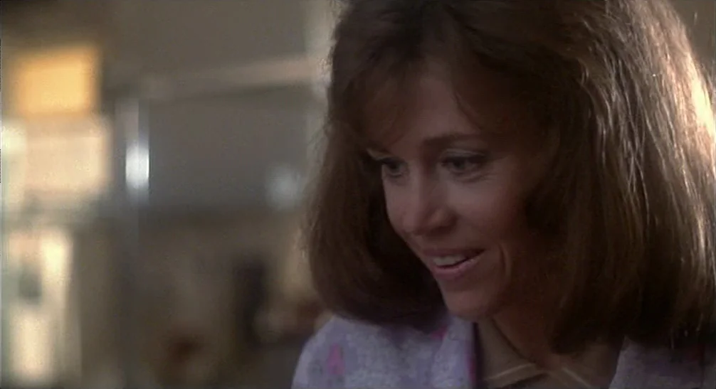 Coming Home (1978) movie still: closeup — An interior residential space features a window with blurred light entering the frame. A woman with brown…