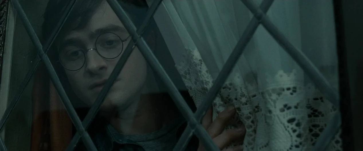 Harry Potter & The Deathly Hallows Part 1 (2010) movie still: closeup — A close-up of a young man looking through a leaded diamond-pane glass…