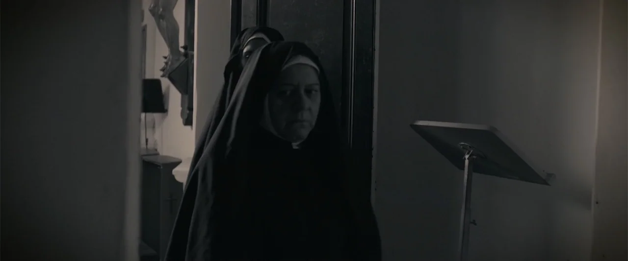 I Trust in You (2016) movie still: medium — An interior stone corridor in a church with a metal music stand nearby. Two nuns in habits stand in the…
