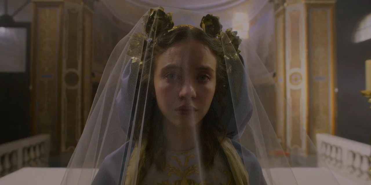 Immaculate (2024) movie still: closeup — An ornate interior space features vaulted ceilings and classical architectural columns. A young woman…