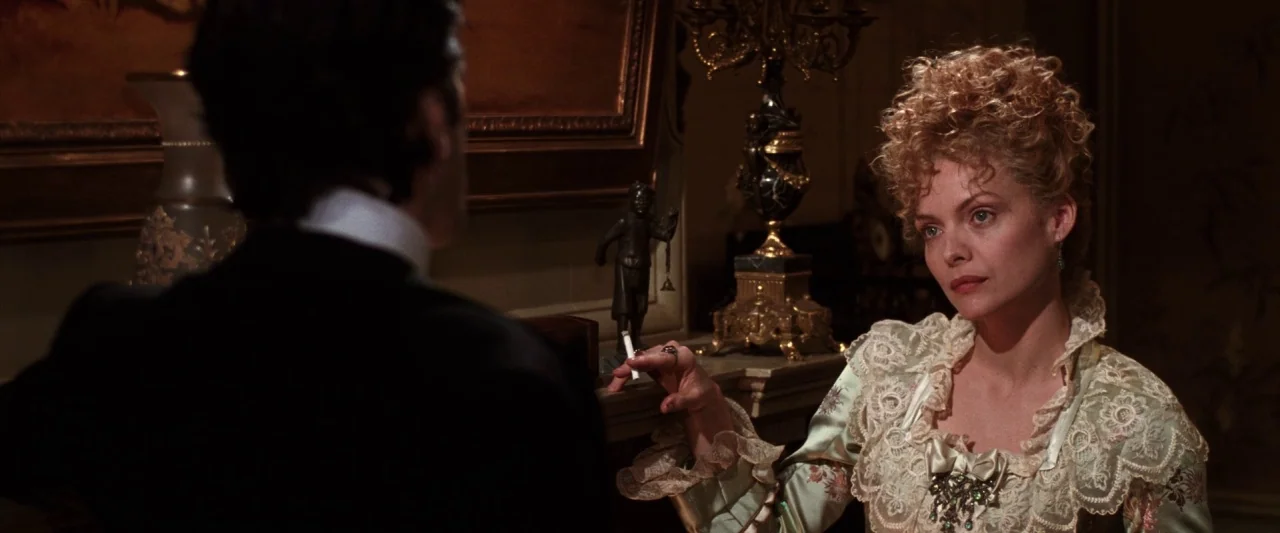 The Age of Innocence (1993) movie still: medium — A dimly lit room decorated in late 19th-century style with ornate furniture and paintings. A woman…