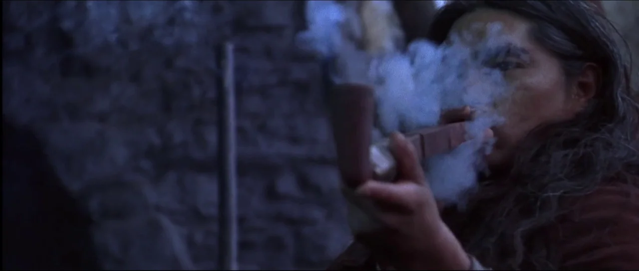 Ravenous (1999) movie still: closeup — An interior space with rough stone walls provides the dark backdrop for the figure. A person with dark hair…