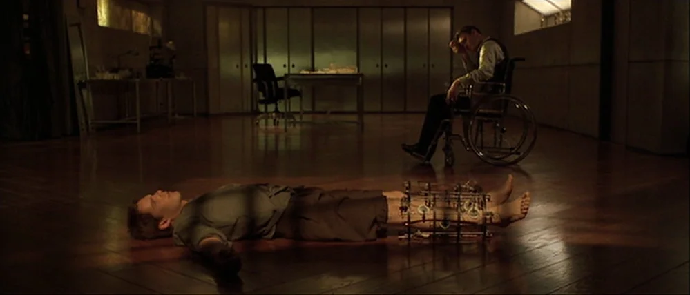 Gattaca (1997) movie still: wide — A spacious room features polished wooden floors and a series of minimalist wall cabinets. One man rests on the…