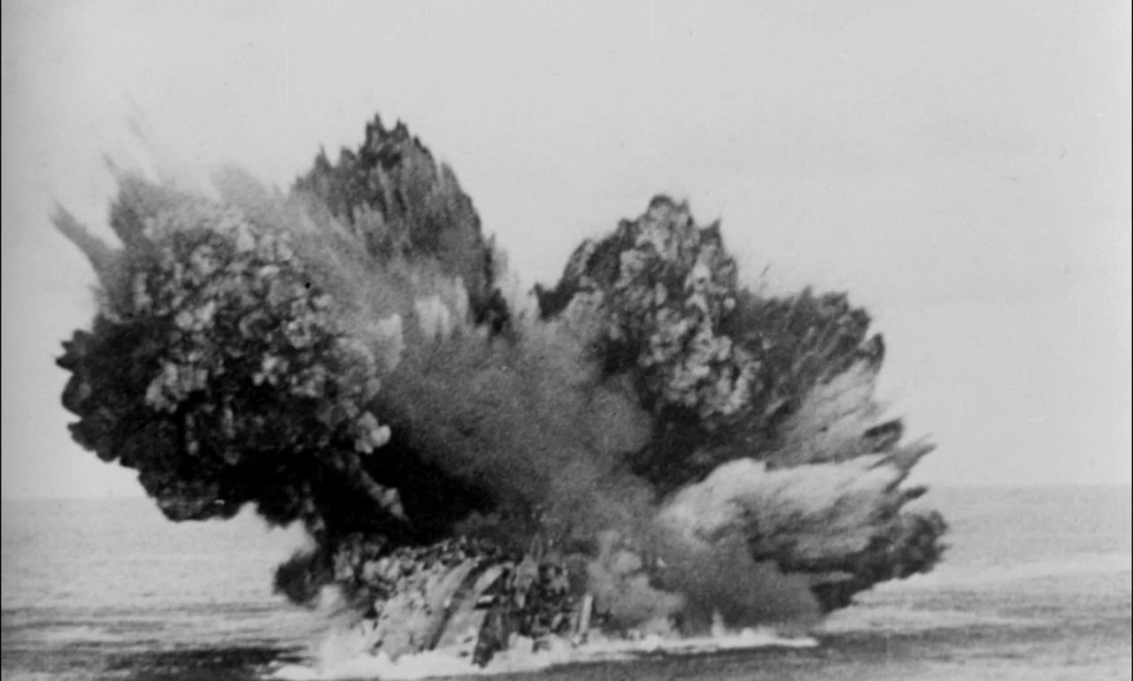 King & Country (1964) movie still: wide — A massive plume of smoke and fire rises from a ship in the ocean. The explosion billows outward against a…