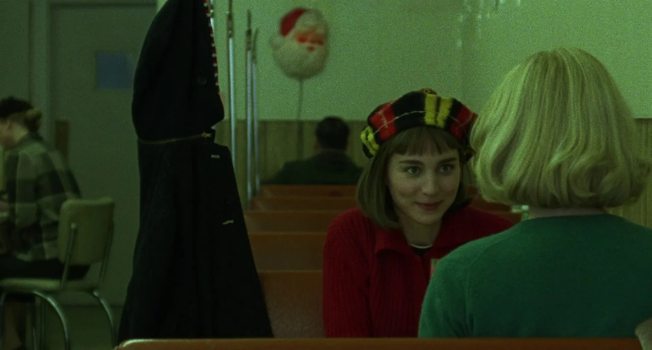 Carol (2015) movie still: medium — A booth in a diner with wood paneling and a festive Santa mask decoration. Two women sit across from one another…