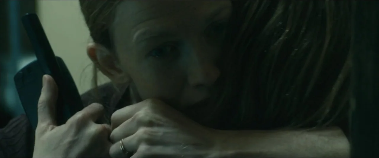 World War Z (2013) movie still: closeup — A dimly lit interior space with muted greenish color tones. A woman embraces another person while holding…