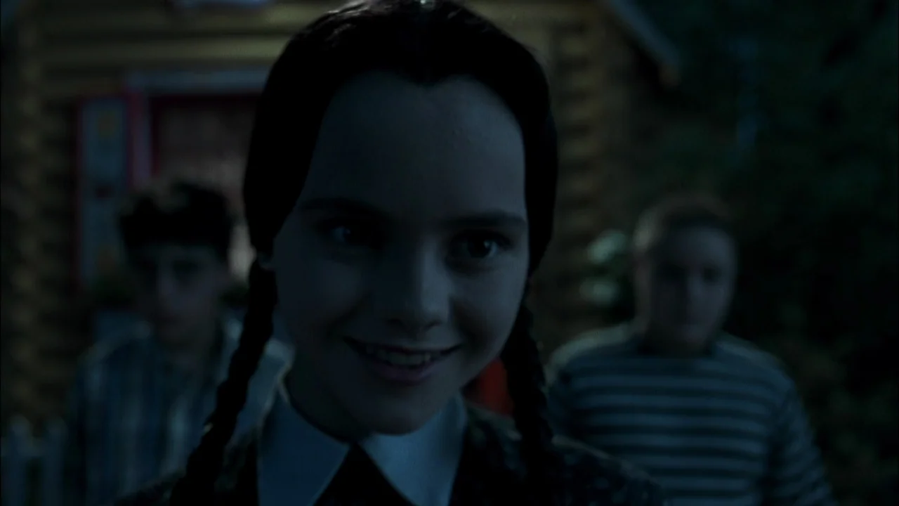 Addams Family Values (1993) movie still: closeup — A dark outdoor scene at night featuring a girl with braided hair. The girl stands in the…
