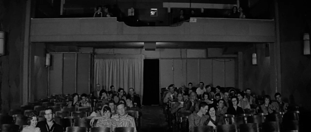 Hud (1963) movie still: wide — An audience sits in a dimly lit, vintage movie theater with an upper balcony section. Rows of empty and occupied…