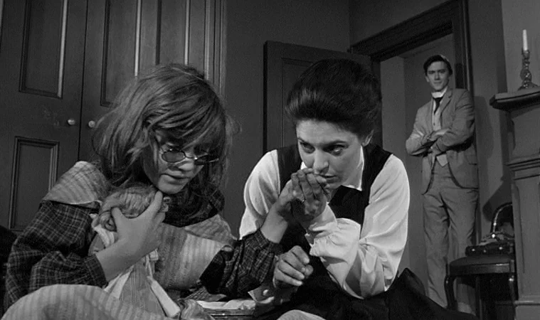 The Miracle Worker (1962) movie still: medium — A dimly lit Victorian parlor features dark wood doors and a fireplace mantel. A woman sits on the…