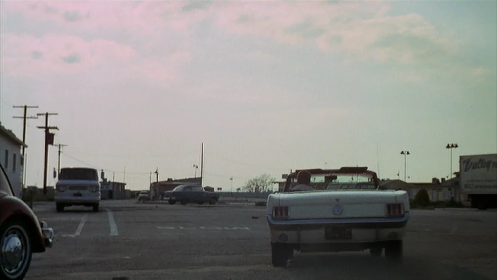 Targets (1968) movie still: wide — A spacious paved parking lot features several vintage automobiles under an overcast afternoon sky. A white…