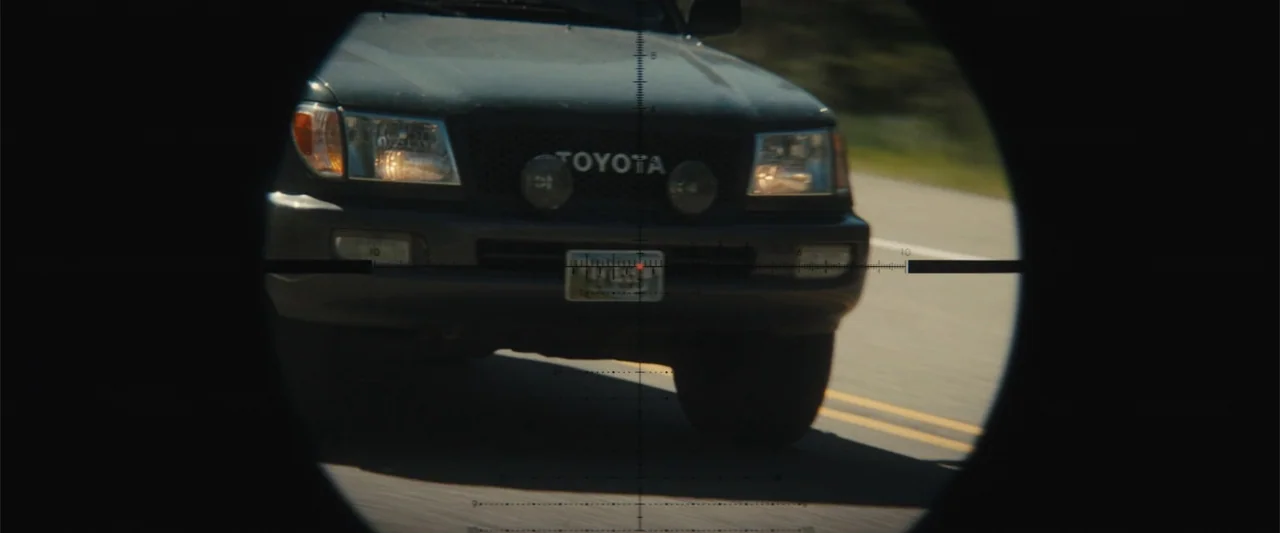 Those Who Wish Me Dead (2021) movie still: medium — A dark Toyota pickup truck moves toward the camera on an asphalt road. A black circular scope…