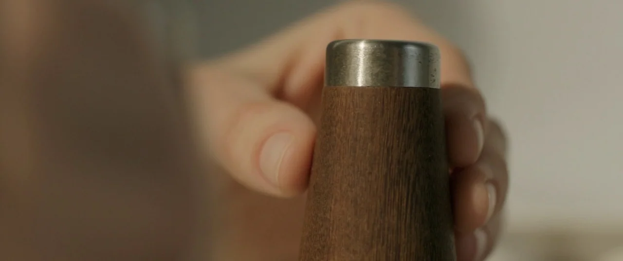 On Body and Soul (2017) movie still: closeup — A wooden pepper grinder with a brushed metal top sits in the foreground. A human hand reaches out…