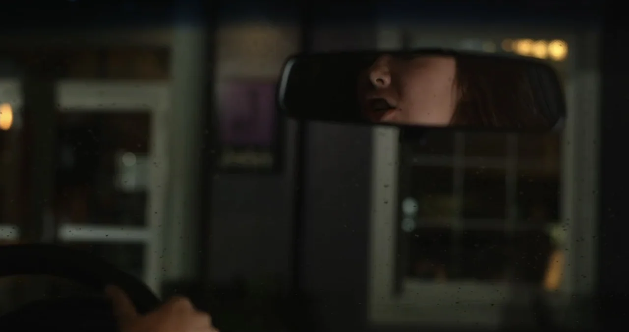Faith, Love & Chocolate (2018) movie still: closeup — The interior of a vehicle at night with a rain-speckled windshield. A young woman is visible…