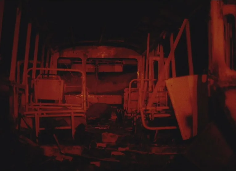 A Visitor to a Museum (1989) movie still: establishing — The interior of a bus features metal seating frames and debris on the floor. Dim red light…