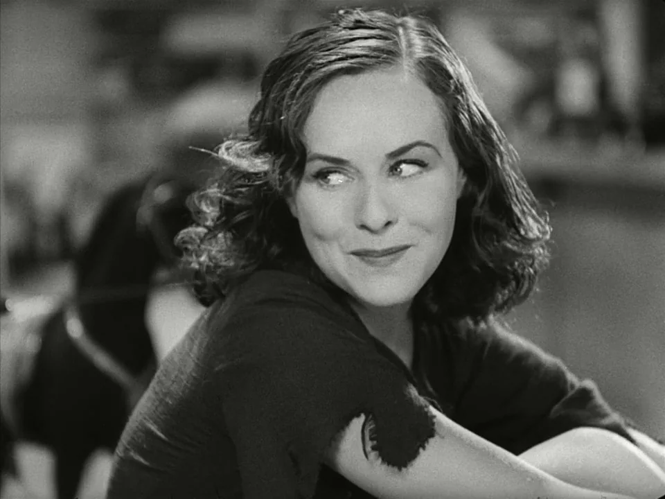 Modern Times (1936) movie still: closeup — A woman turns her head to look over her shoulder in a dimly lit area. The background shows blurred…