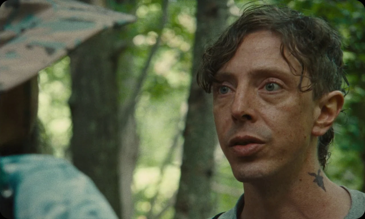 Vulcanizadora (2024) movie still: closeup — A man stands outdoors amidst a dense collection of trees with blurred green foliage. The man is looking…