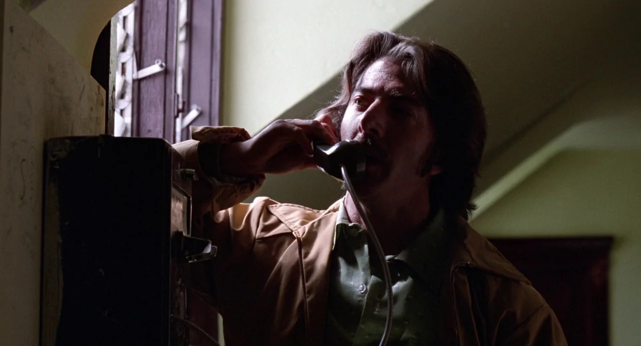 Straight Time (1978) movie still: medium — A man stands in an interior hallway with pale green walls and a window. He holds a vintage wall-mounted…