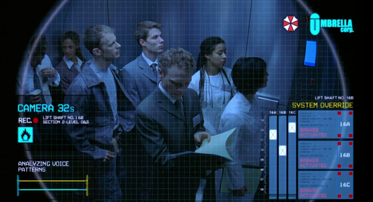 Resident Evil (2002) movie still: medium — Several corporate employees in business attire stand inside a brightly lit metal lift car. A digital…