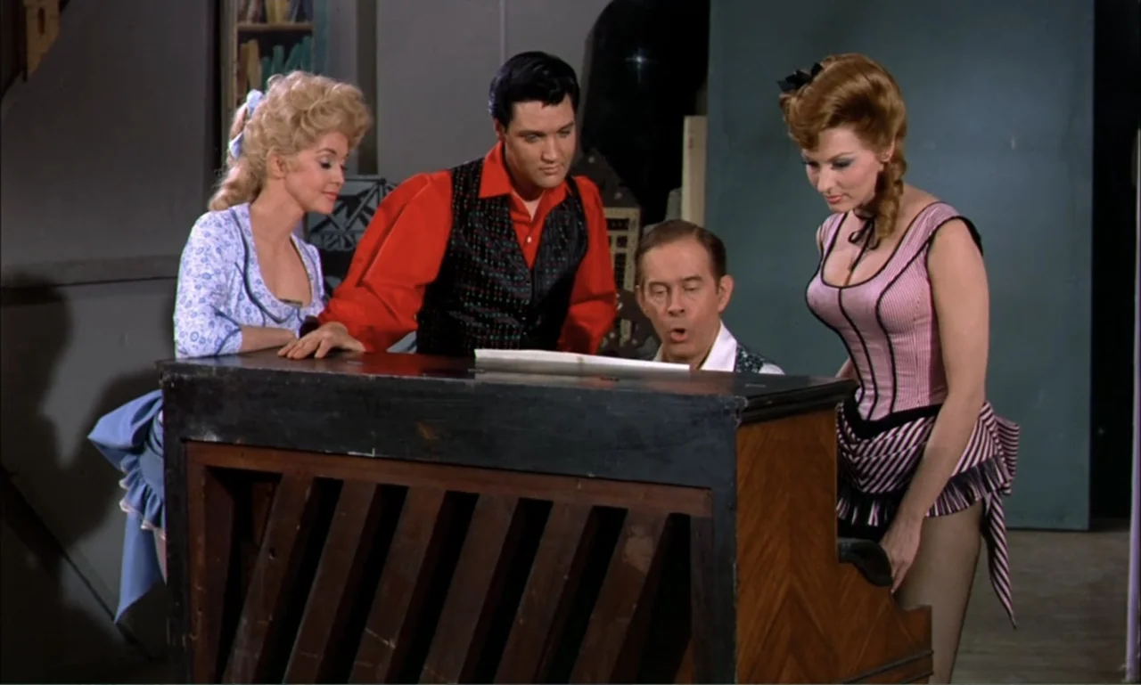 Frankie and Johnny (1966) movie still: medium — A room with a piano serves as a gathering space for four people. Three people stand around a central…