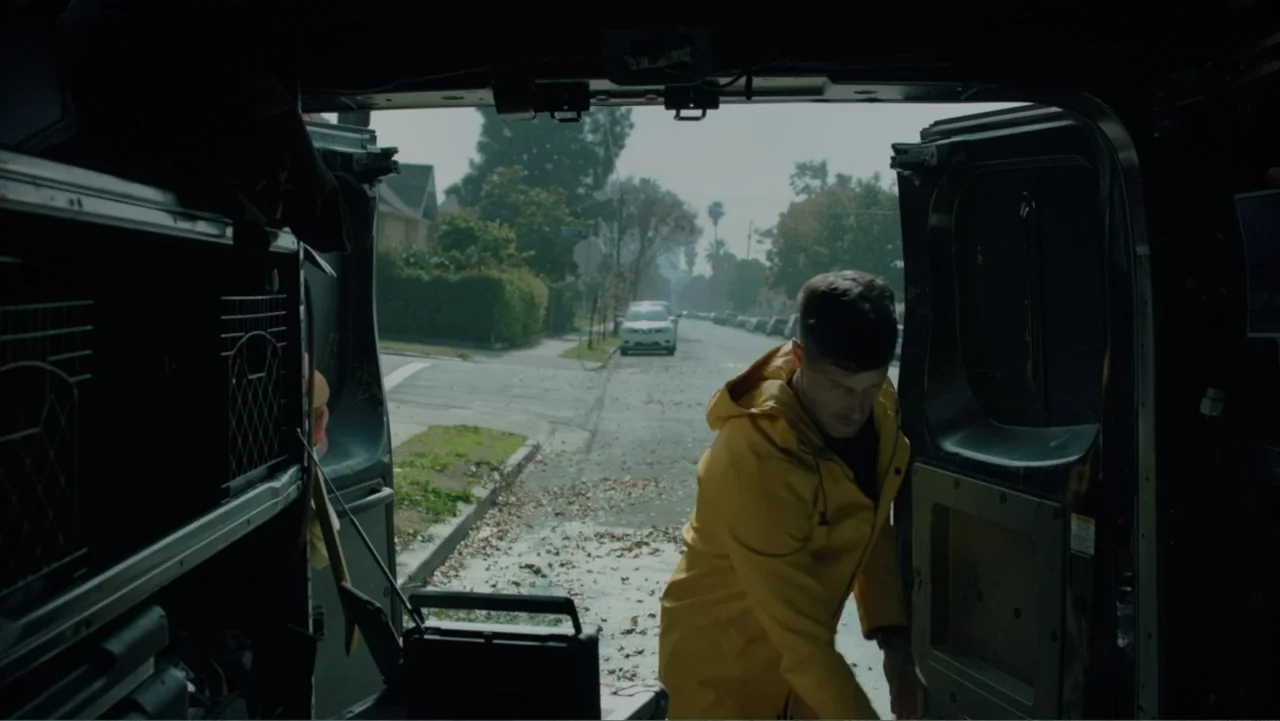 Storm Damage (2000) movie still: medium — The interior of a work van opens to a quiet suburban residential street. A man wearing a yellow jacket…