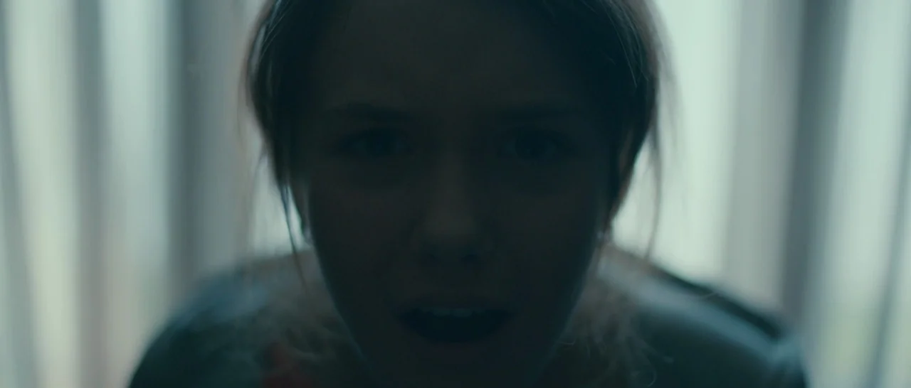 Arrival (2016) movie still: closeup — A close-up of a young woman's face silhouetted against a bright, out-of-focus background. The subject leans…