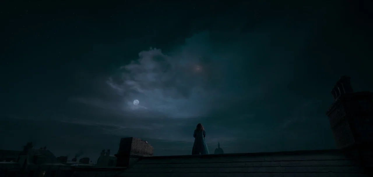 Peter Pan & Wendy (2023) movie still: wide — A person stands on a dark, tiled rooftop against a massive night sky. The moon shines through heavy…