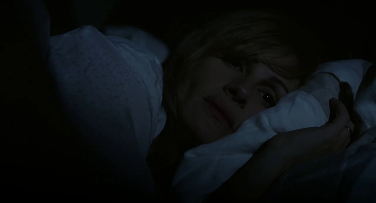 Closer (2004) movie still: closeup — A person lies in a dark room under white blankets in a bed. The individual rests their cheek on a soft pillow…