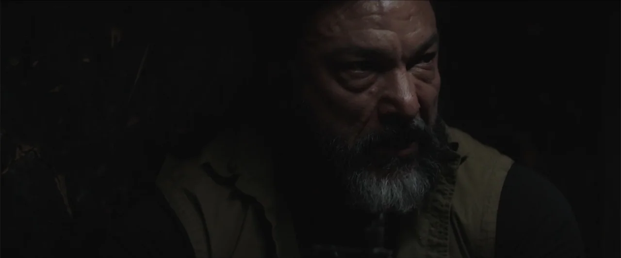 Redemption Day (2021) movie still: closeup — A dimly lit interior space with the subject obscured by heavy surrounding shadow. An older man with a…