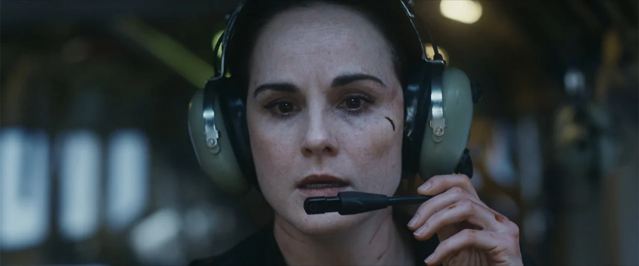 Flight Risk (2025) movie still: closeup — A dark, cramped military or aviation interior with blurred background controls and mechanical elements. A…