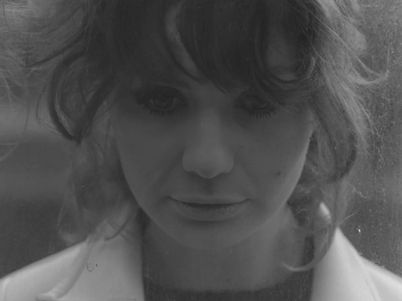 The Baby Carriage (1963) movie still: closeup — A woman stares through a glass surface that contains dust particles and light reflections. The…
