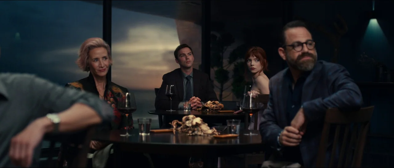 The Menu (2022) movie still: medium — A high-end restaurant with floor-to-ceiling windows overlooking a dark ocean at twilight. Four individuals…