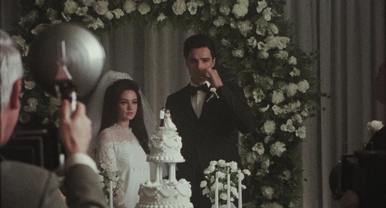 Priscilla (2023) movie still: medium — A formal indoor reception area is decorated with abundant white floral arrangements. A bride and groom stand…