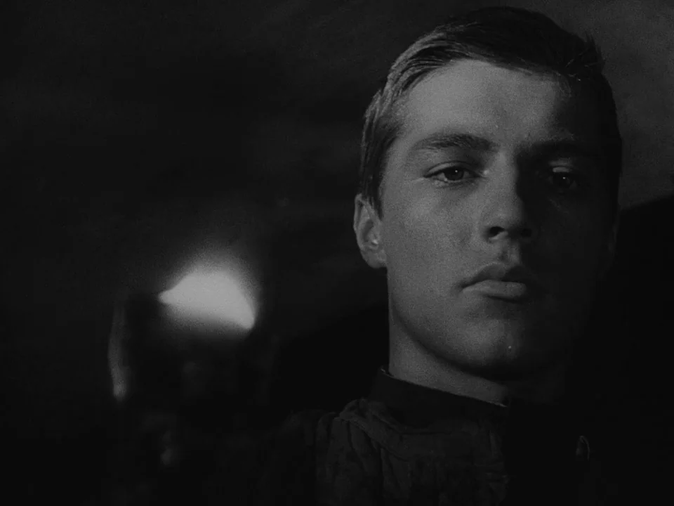 Ivan’s Childhood (1962) movie still: closeup — A dark stone space with a light source glowing off-screen in the foreground. A young man stares…