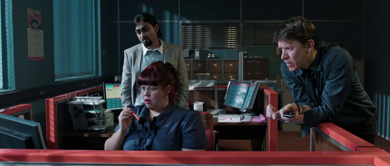 The Voices (2014) movie still: medium — A modern workspace with red partition dividers and beige filing cabinets in the background. Three coworkers…