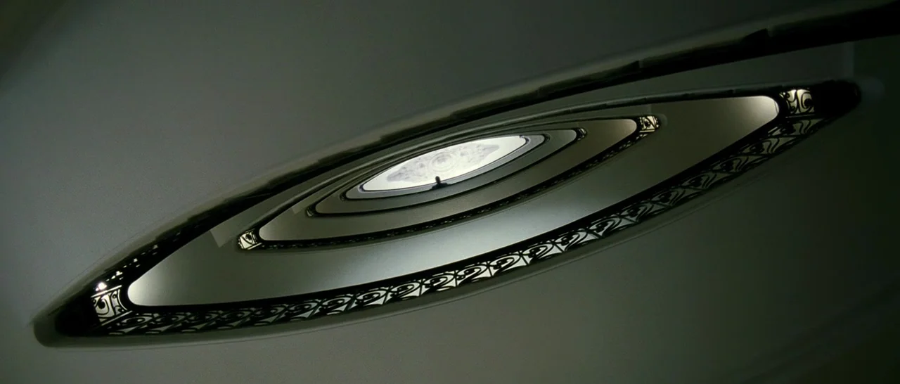 The Great Beauty (2013) movie still: establishing — An oval-shaped architectural stairwell with white walls and ornate wrought iron banisters. A…
