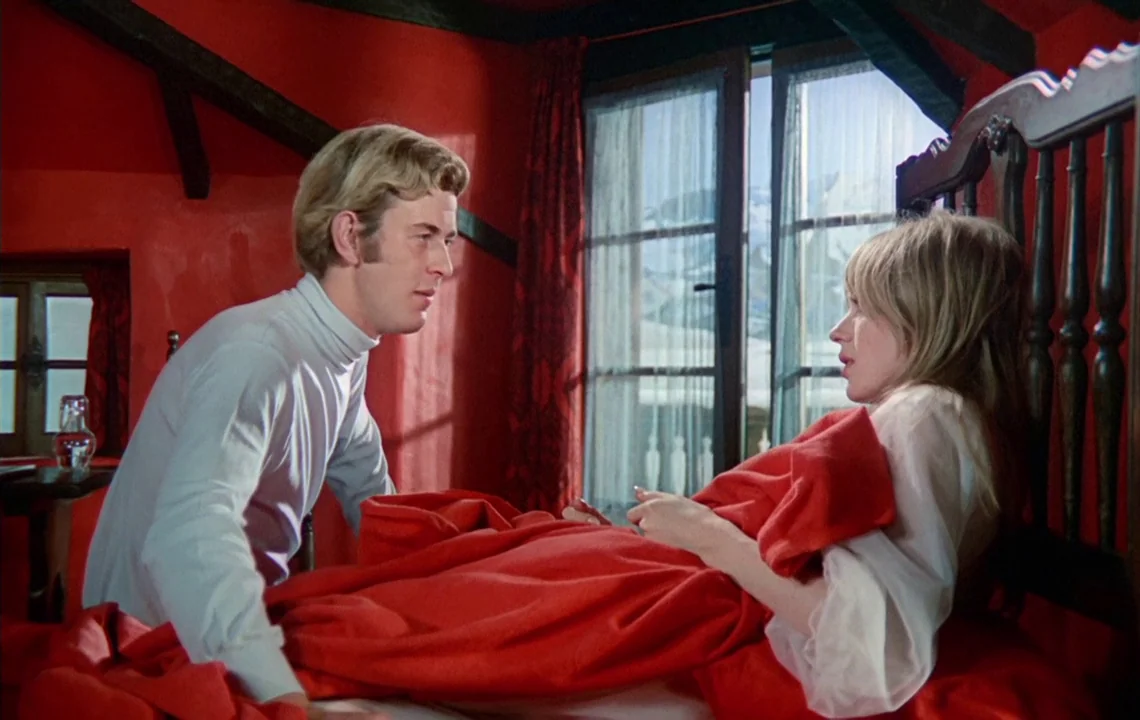 The Girl on a Motorcycle (1968) movie still: medium — A room with bright red walls and exposed wooden beams contains a bed. A blonde man sits over a…