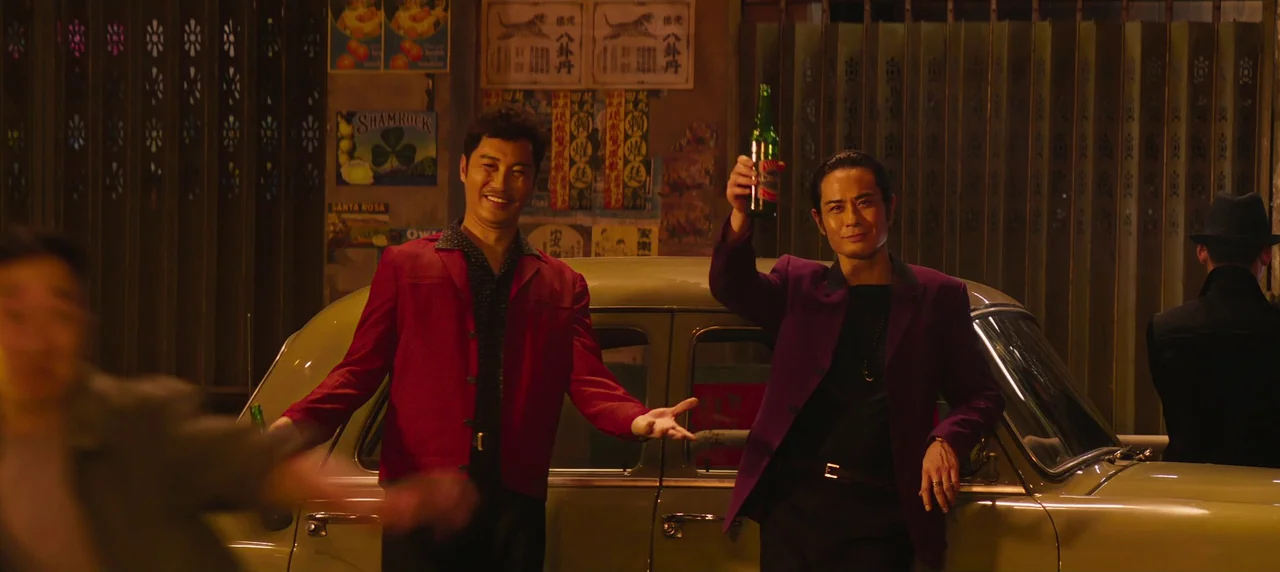Master Z: The Ip Man Legacy (2018) movie still: medium — A narrow outdoor passage features a vintage beige sedan parked against posters and metal…