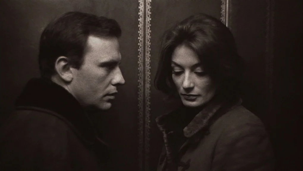 Un Homme et Une Femme (1966) movie still: medium — A dark elevator interior features wood paneling and a vertical decorative metallic trim. A man in…