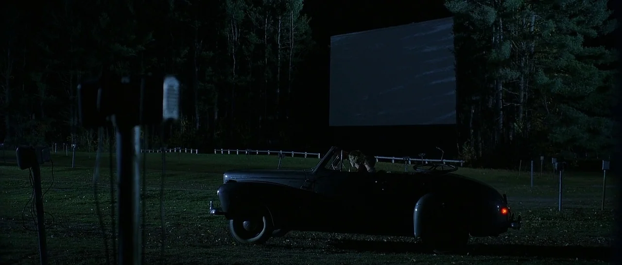 The Cider House Rules movie still: wide — A drive-in movie theater at night with an empty screen looming over a field. A vintage convertible car…