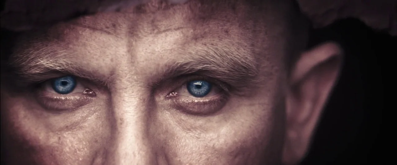 Skyfall (2012) movie still: closeup — A close-up view of a man's face from the nose up against a dark background. He is staring directly forward…