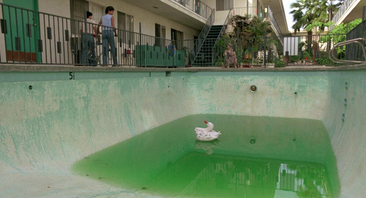 The Karate Kid (1984) movie still: wide — An empty motel pool with green water sits in front of a two-story building. Three people are positioned…