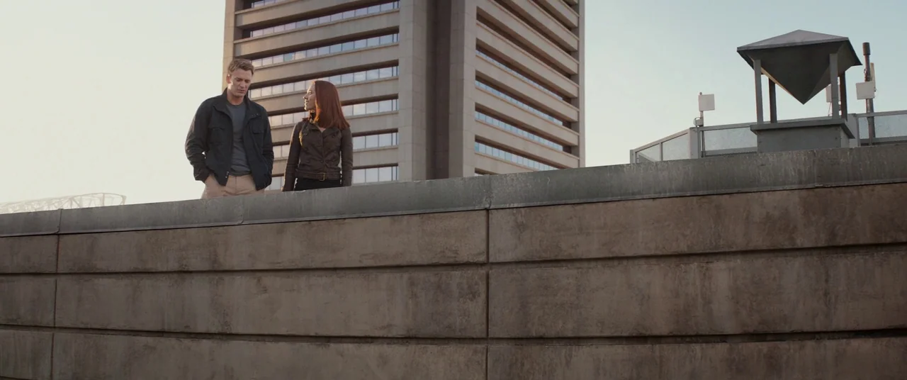 Captain America: The Winter Soldier (2014) movie still: wide — A flat concrete rooftop features a tall, tiered modernist building in the background.…