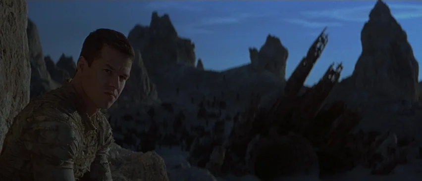Planet of the Apes (2001) movie still: medium — A man stands atop a rocky cliff in a vast desert landscape at night. Jagged rock pillars rise from…