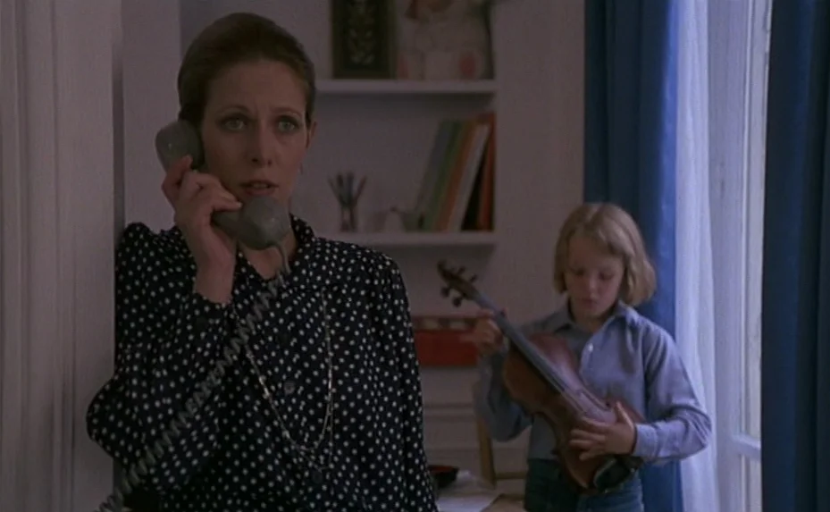 Love on the Run (1979) movie still: medium — A residential room features a white bookshelf with colorful spines and a window with blue curtains. A…