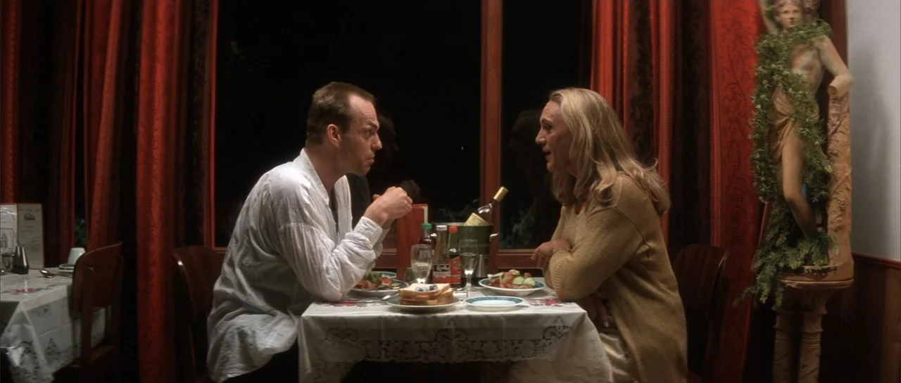 The Adventures of Priscilla, Queen of the Desert (1994) movie still: medium — A dimly lit restaurant interior features red curtains framing a dark…