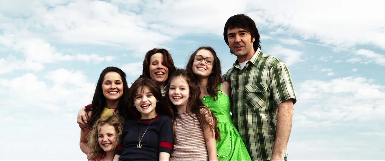 The Conjuring (2013) movie still: medium — A group of six people standing together outdoors against a clear, cloudy sky. The family members are…