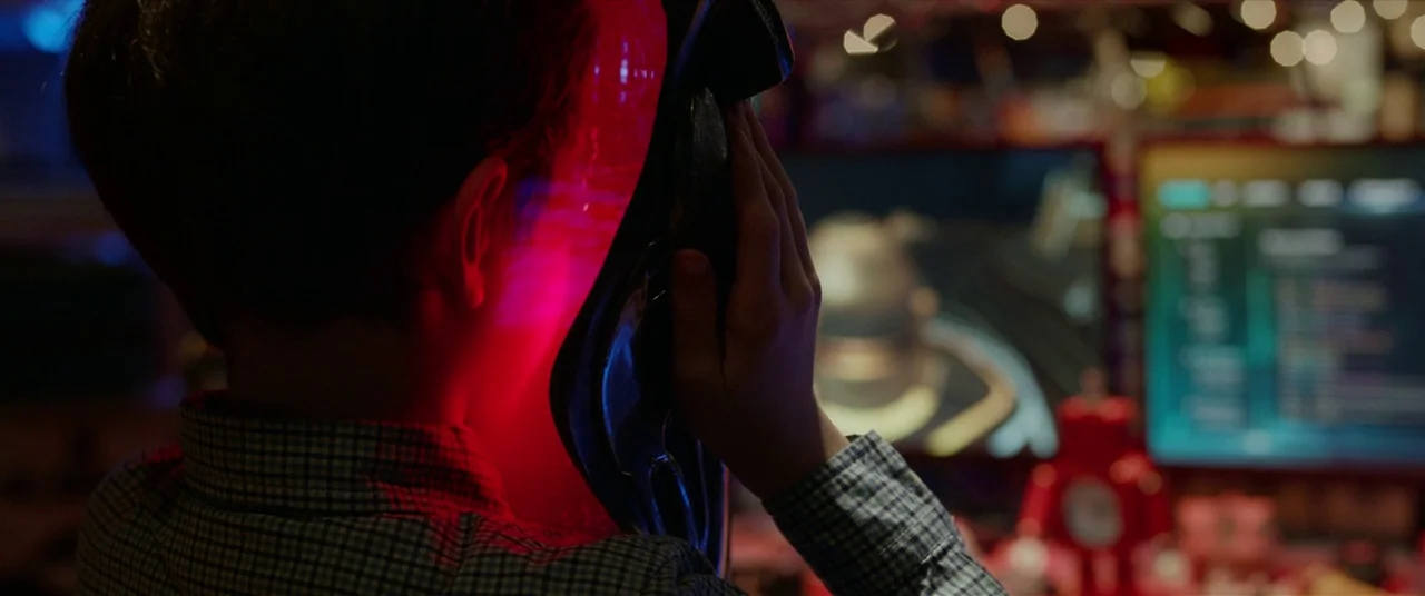 The Predator (2018) movie still: closeup — A dark space lit by computer monitors displays code and graphics on screens. A young boy holds an object…