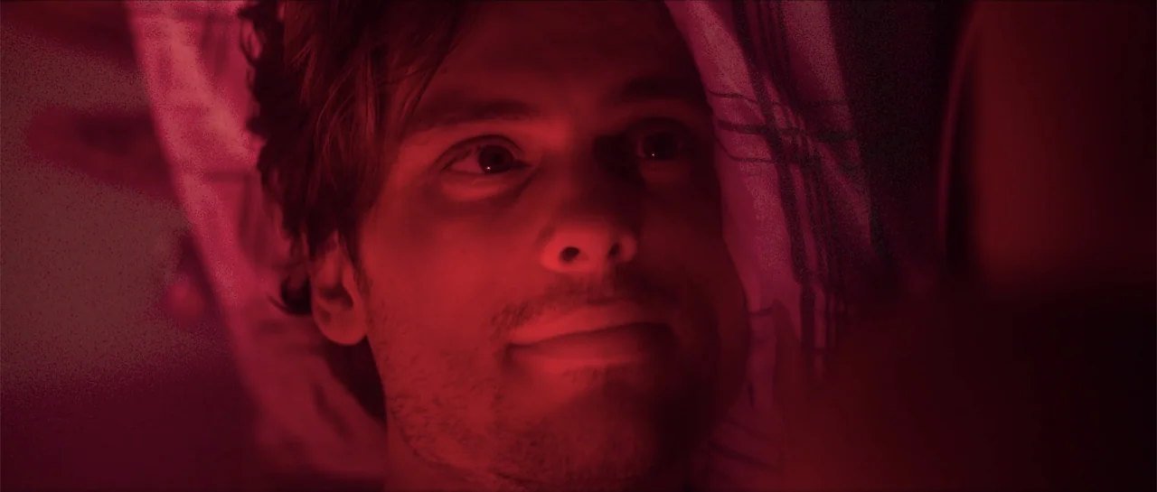 68 Kill (2017) movie still: closeup — A bedroom at night with a patterned pillow visible behind a person's head. A man with stubble lies down with…