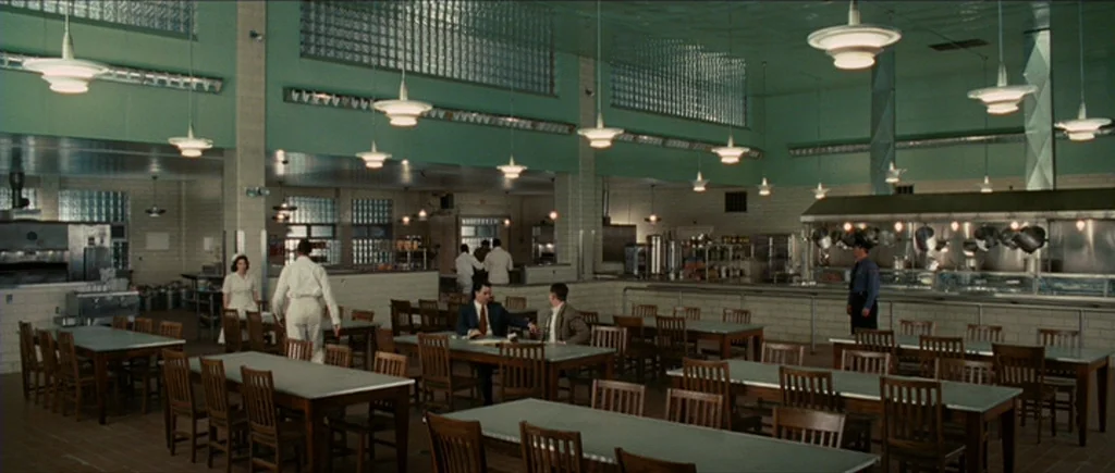 Shutter Island (2010) movie still: wide — A spacious, mint-green cafeteria features long rows of wooden tables and chairs. Several individuals…