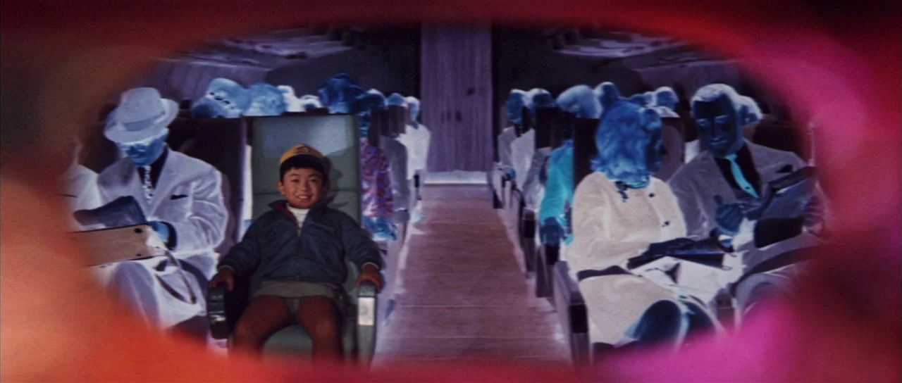 All Monsters Attack (1969) movie still: medium — An airplane cabin with rows of passengers seated on either side of the aisle. A young boy sits in…